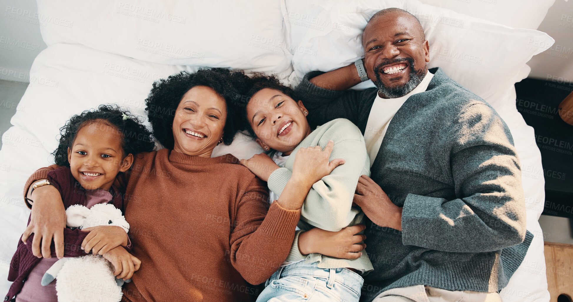Buy stock photo Portrait, cuddle and parents with children in bed, support and affection for relationship development. Above, African family and happy people with girls for connection, bonding and teddy bear in home