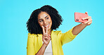 Smile, peace sign and selfie of woman in studio for social media, profile picture or post. Entrepreneur, v hand emoji and female person with happy memory for influencer update on blue background