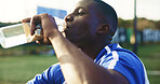 Soccer, break and black man with drinking water for hydration, wellness and training outdoor. Football, thirsty and sports person or player with liquid bottle, resting and practice on field for game