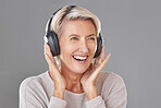 One happy mature woman isolated against a grey background in a studio and wearing headphones to listen to music. Smiling caucasian senior enjoying the loud music and looking youthful and playful