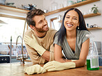 Happy young interracial couple cleaning their home. Young man and woman wearing gloves and using cleaning detergents while doing chores together at home.