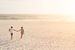 Young couple holding hands walking towards sunset on empty beach