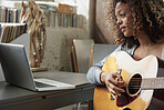 Attractive mixed race young girl learning to play guitar using laptop computer 