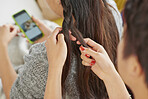 Multi racial girl friends brading hair smiling using mobile phone hanging out on sofa 