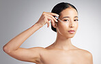 Studio Portrait of a beautiful mixed race woman applying a soothing face serum to her radiant smooth face while posing against a grey background. Hispanic woman with flawless skin using essential oil