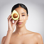 Studio Portrait of a beautiful young mixed race woman holding a sliced avocado. Hispanic model with glowing skin holding a fruit against a grey copyspace background
