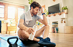 One fit young caucasian man wiping sweat off forehead with a towel while taking a break from exercise at home. Tired guy drinking water to quench thirst and cool down after training workout