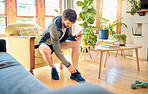 One fit young caucasian man getting dressed for exercise workout while listening to music with earphones on a cellphone at home. Guy sitting on a chair putting on sports shoe sneakers while getting ready to go to gym for training