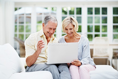 Buy stock photo A delighted senior couple using a laptop while relaxing in their lounge