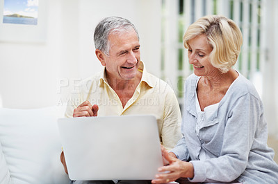 Buy stock photo A delighted senior couple using a laptop while relaxing in their lounge
