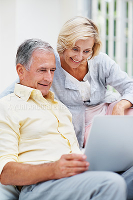 Buy stock photo A smiling senior couple watching a movie on their laptop while relaxing in the lounge