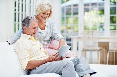 Buy stock photo A senior couple browsing photos on social media on a tablet in their lounge