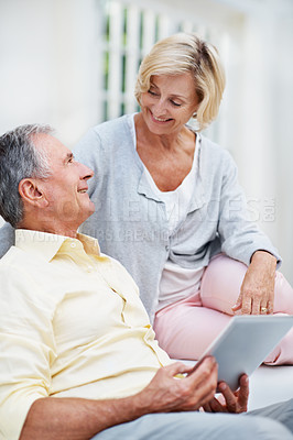 Buy stock photo A senior couple looking at one another while using a tablet at home