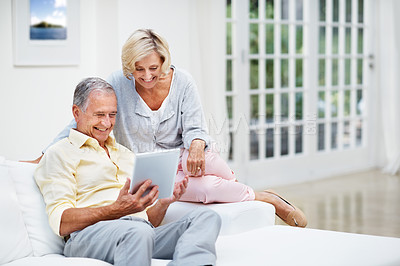 Buy stock photo A senior couple browsing photos on social media on a tablet in their lounge
