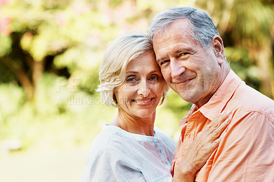 Buy stock photo A smiling senior couple standing outdoors and embracing one another on a bright summer's day
