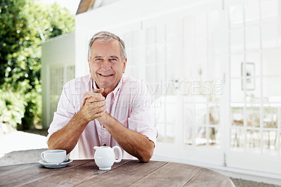 Buy stock photo A senior man smiling at the camera while sitting outside his house with a cup of coffee in front of him - copyspace