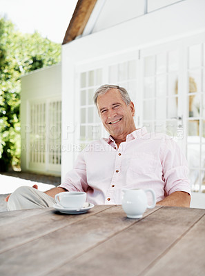 Buy stock photo A senior man smiling at the camera while sitting outside his house with a cup of coffee in front of him - portrait