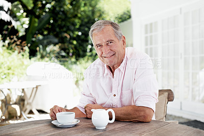 Buy stock photo A senior man smiling at the camera while sitting at a table outside his house with a cup of coffee in front of him - portrait