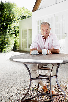 Buy stock photo A senior man smiling at the camera while sitting at a table outside his house with a cup of coffee in front of him