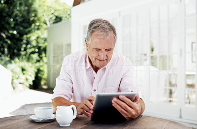 Buy stock photo A smiling senior man sitting outside his home working on a digital tablet 