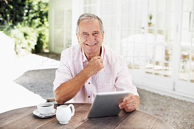 Buy stock photo A smiling senior man holding a digital tablet while sitting outside with a cup of coffee