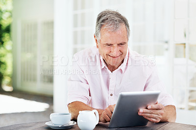 Buy stock photo A smiling senior man working on a digital tablet while sitting outside with a cup of coffee