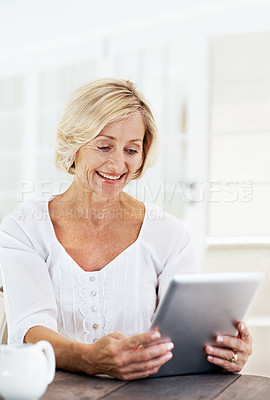 Buy stock photo A smiling senior woman holding a digital tablet while sitting outside with a cup of coffee 
