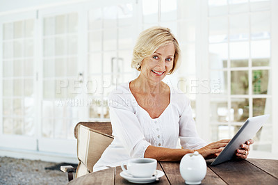 Buy stock photo A smiling senior woman holding a digital tablet while sitting outside with a cup of coffee 