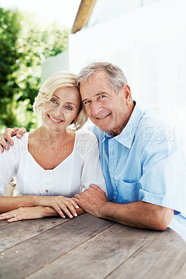 Buy stock photo A loving mature couple smiling at the camera while sitting at a table outside their home