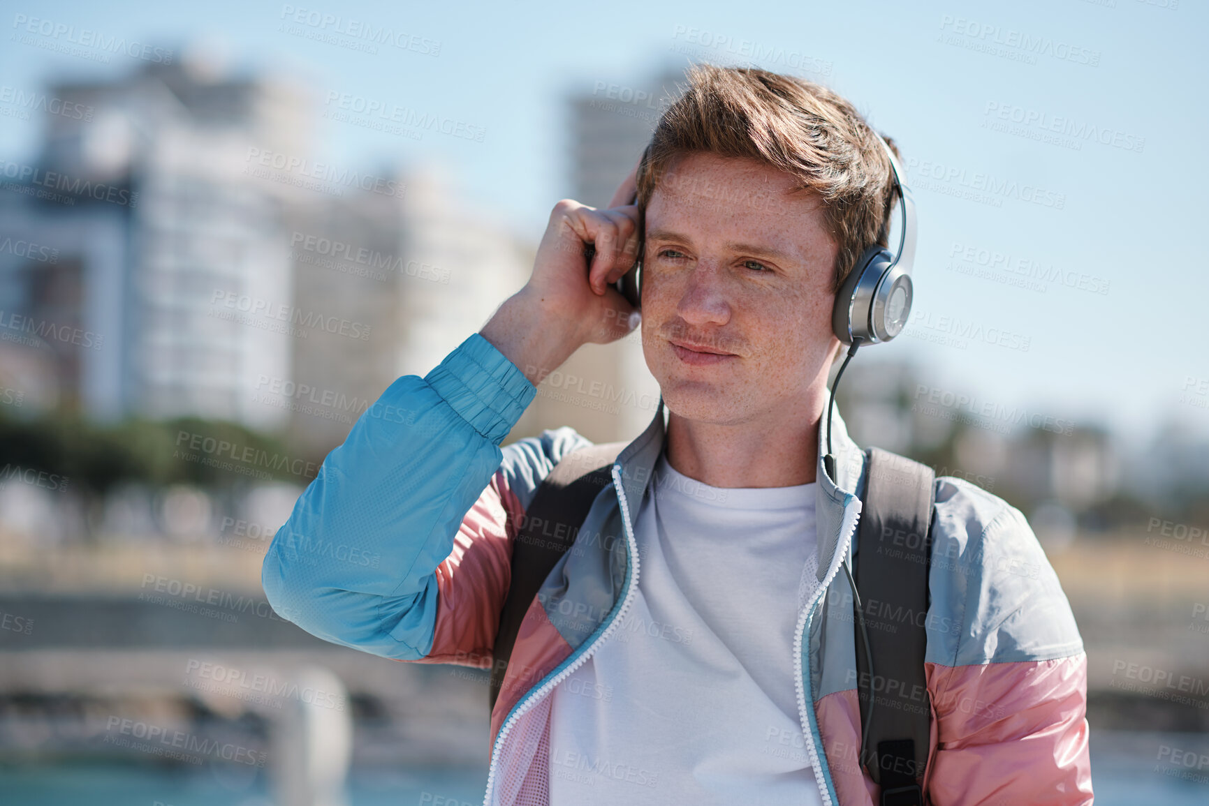 Buy stock photo Headphones, smile and man by beach on holiday with listening to music, playlist or radio. Promenade, audio tech and male person streaming album by ocean on summer vacation, getaway or weekend trip