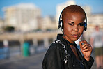 Young african american woman with shaved hair listening to music wearing headphones in city