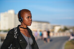 Young african american woman with shaved hair listening to music wearing headphones in city
