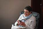 Happy elderly woman using smartphone texting browsing on mobile phone sending messages sitting on couch at home