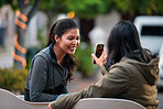 woman showing smartphone to best friend smiling happy looking at mobile phone best friends sitting on bench in city