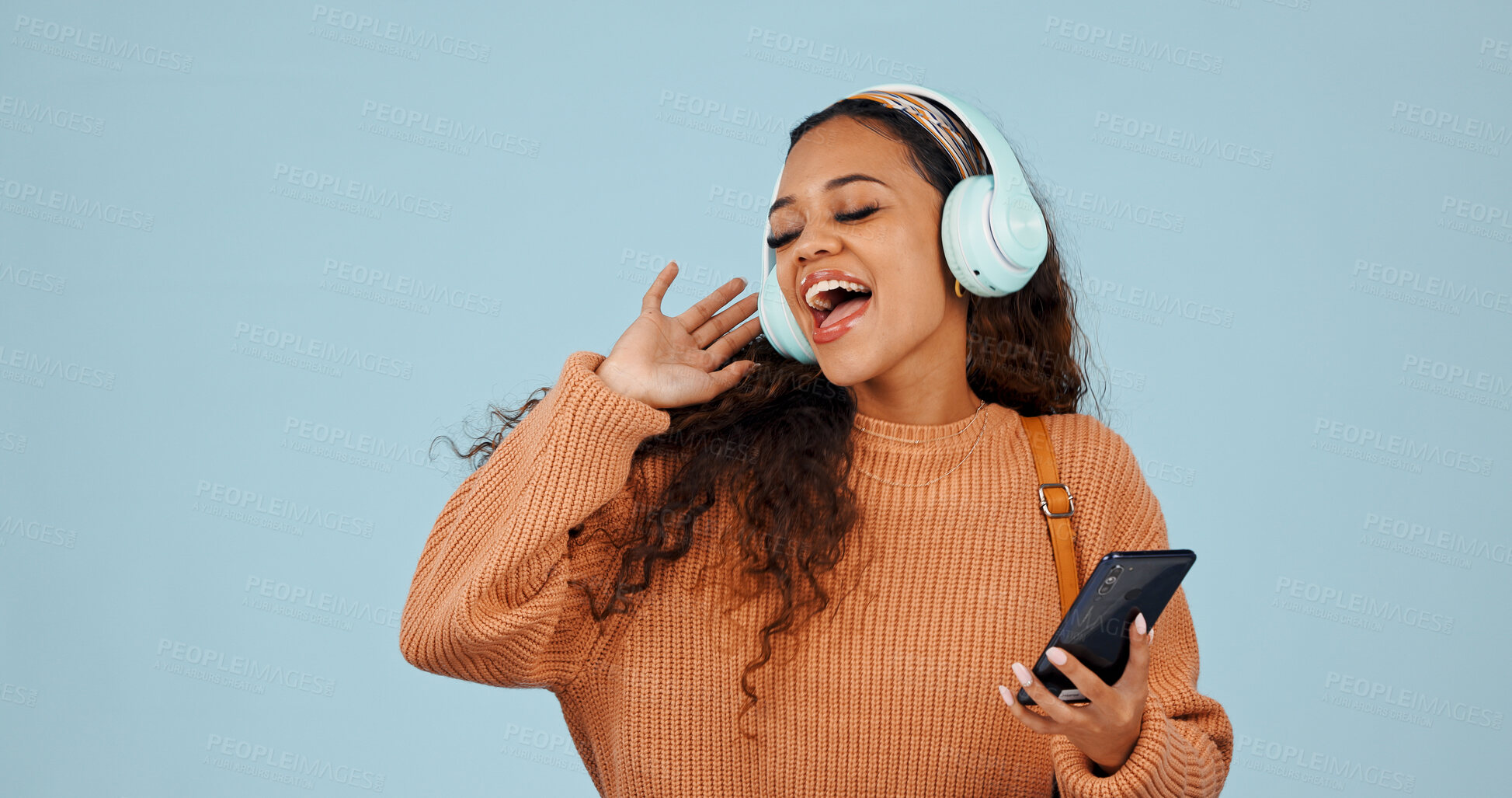 Buy stock photo Phone, headphones and woman in studio with singing, dancing and listening to music or playlist. Happy, cellphone and female person with audio tech for streaming album on mobile app by blue background