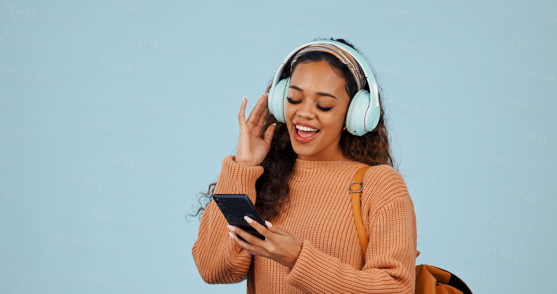 Buy stock photo Phone, headphones and woman in studio with dancing, singing and listening to music or playlist. Space, cellphone and female person with audio tech for streaming album on mobile app by blue background