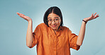 Woman, portrait and shrug in studio with smile, clueless and careless with hands raised for opinion. Girl, gesture and glasses on blue background for doubt, confused and uncertain with body language