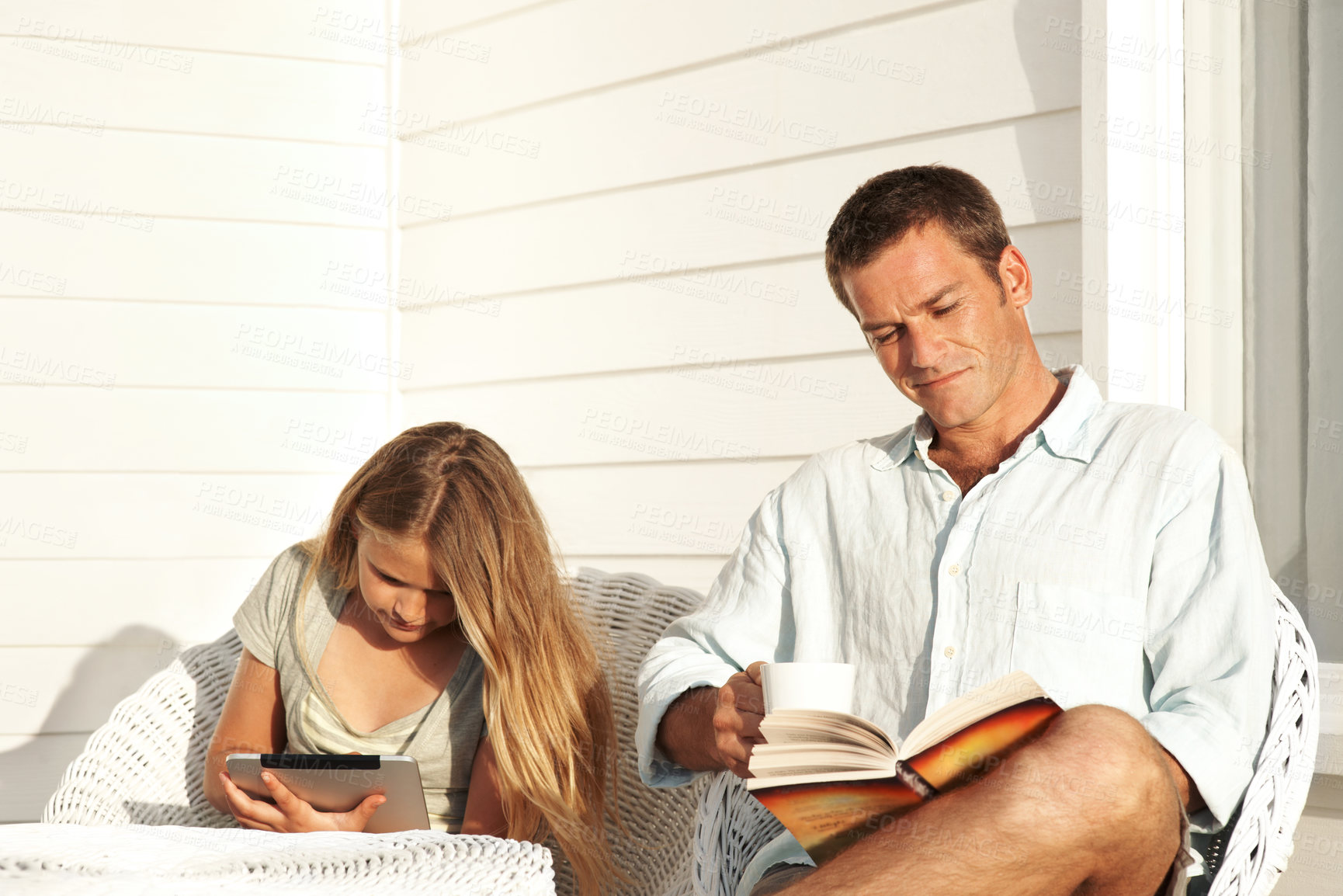 Buy stock photo Man, relax and reading book on patio with child, bonding and literature novel for weekend break. Father, coffee and daughter browsing with tablet, fiction story and information for knowledge at house