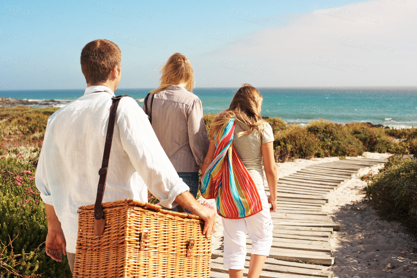 Buy stock photo Back, walking and love with family at beach for summer vacation, bonding and tropical adventure. Holiday getaway, care and picnic basket with parents and child on boardwalk for support and travel