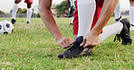 Hands, grass and soccer player tying laces for match, training or exercise outdoor on field. Sports, man and athlete with togs for preparing for football game, workout or practice for championship.