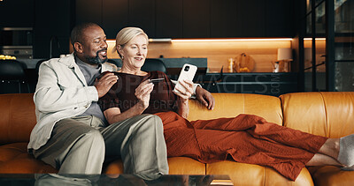 Buy stock photo Mature, couple and credit card in home with phone, plan holiday or payment of flight ticket for travel. Happy, interracial marriage and people on sofa with online banking, tech and vacation expenses.