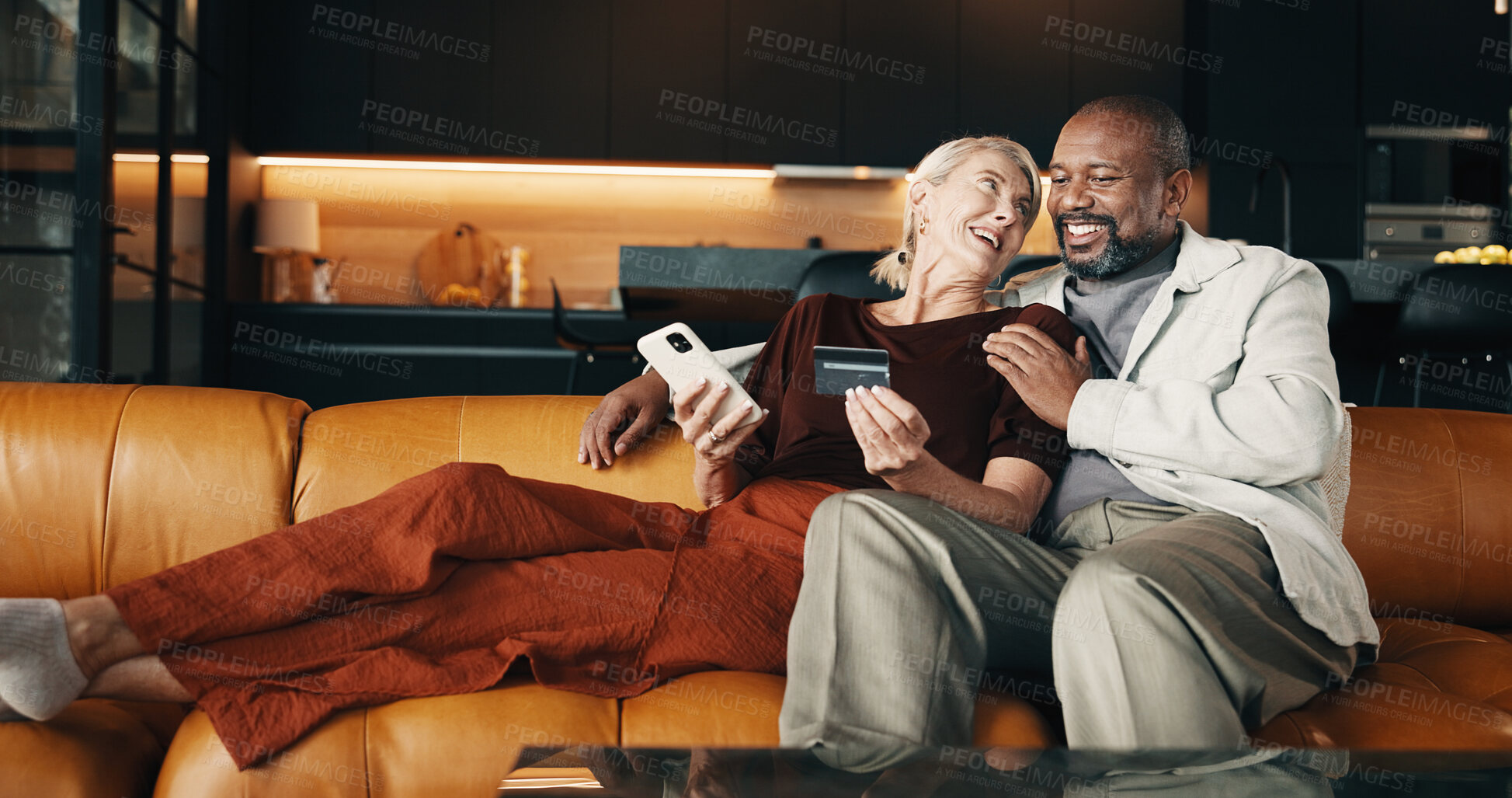 Buy stock photo Mature, couple and credit card in house with phone, plan holiday or payment for booking trip. Happy, interracial marriage and people in lounge with online banking, technology and travel expenses