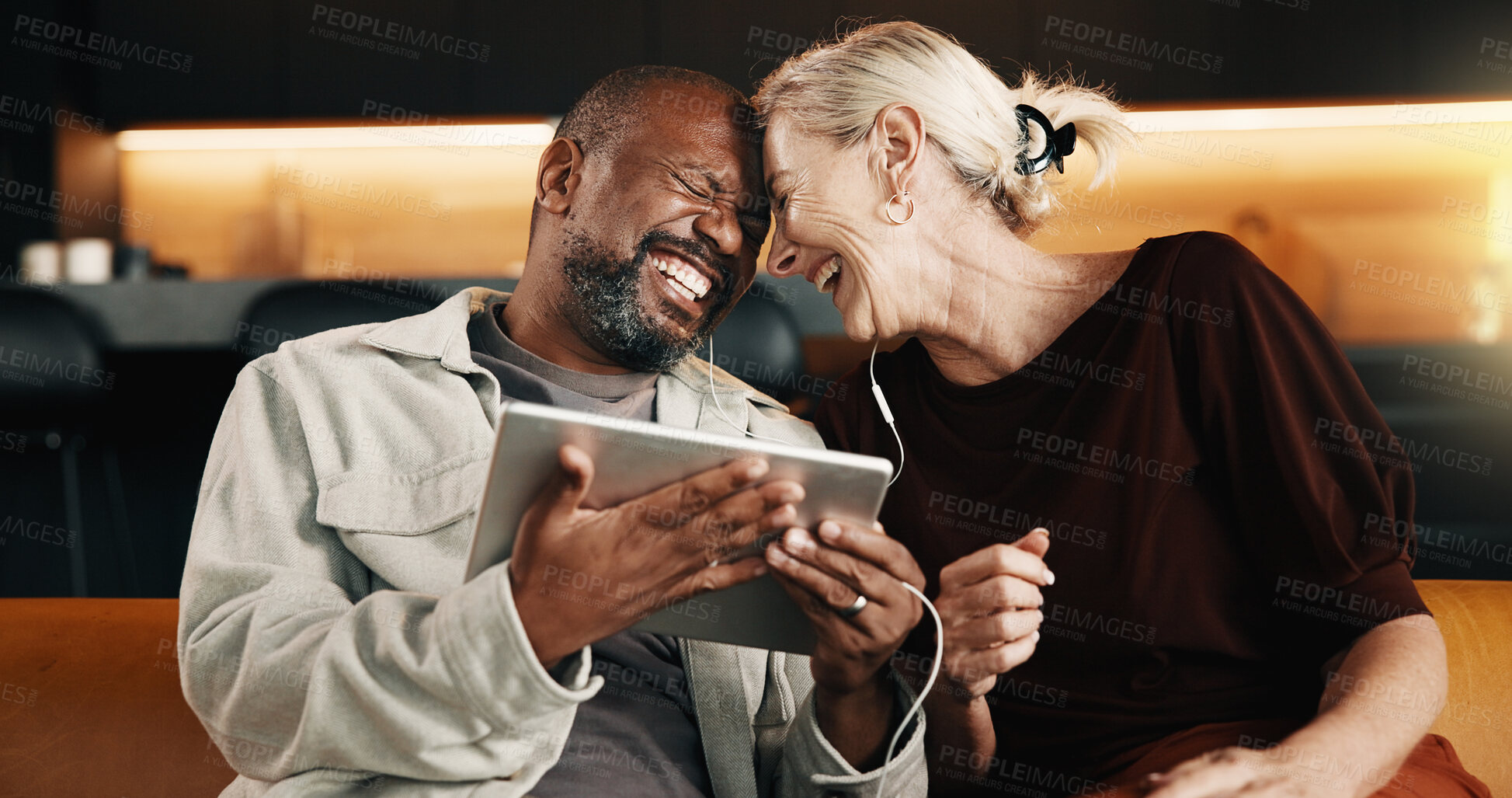 Buy stock photo Mature, couple and laugh with earphones for tablet, watching funny movie and love for bonding together. Happy, interracial marriage and people in home with audio tech, streaming comedy show and joke.