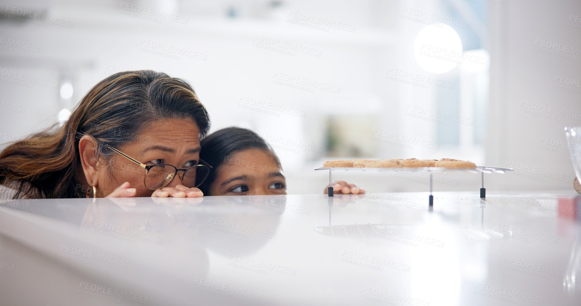 Buy stock photo Grandmother, child and sneaky by kitchen counter for cookies, bonding or stealthy for sweet treats. Hungry, girl and senior woman in home with sugar craving, hide or sly with grandchild for biscuits.
