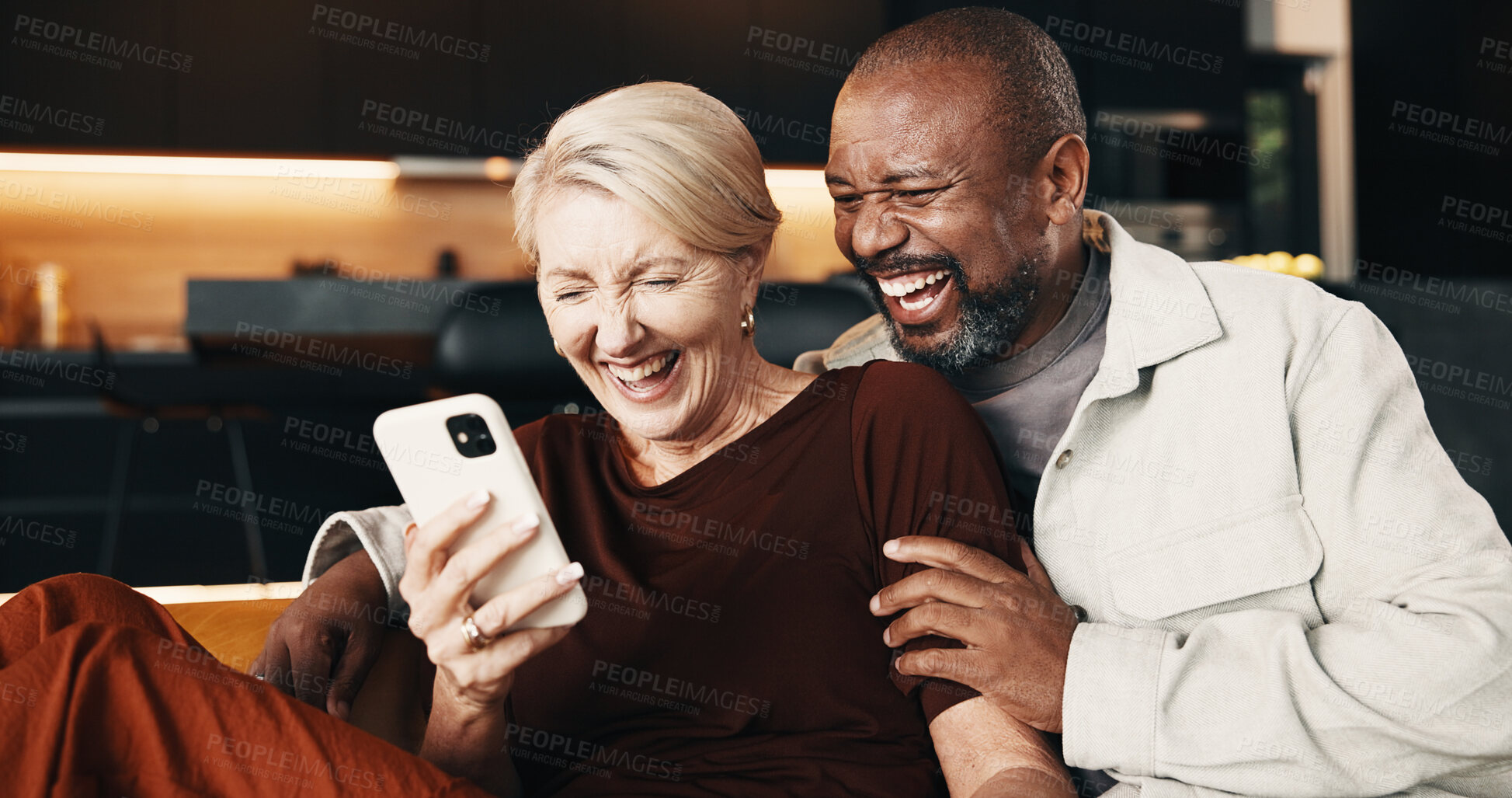 Buy stock photo Interracial couple, phone and laugh with hug for funny joke, mobile app and conversation in home. Mature people, communication and smile for streaming entertainment on tech for humor on social media