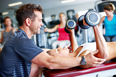 Buy stock photo Shot of a trainer spotting a young woman while she uses dumbbells