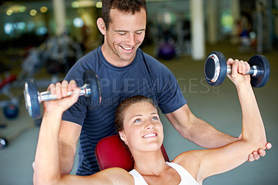 Buy stock photo Shot of a trainer spotting a young woman while she uses dumbbells