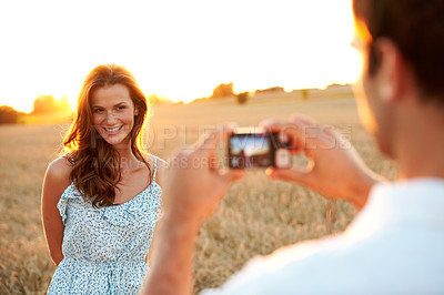 Buy stock photo Woman, sunset and camera with couple in field, photography or memory of honeymoon. Female person, smile and nature with man and digital tech for picture taking, anniversary trip and relationship 