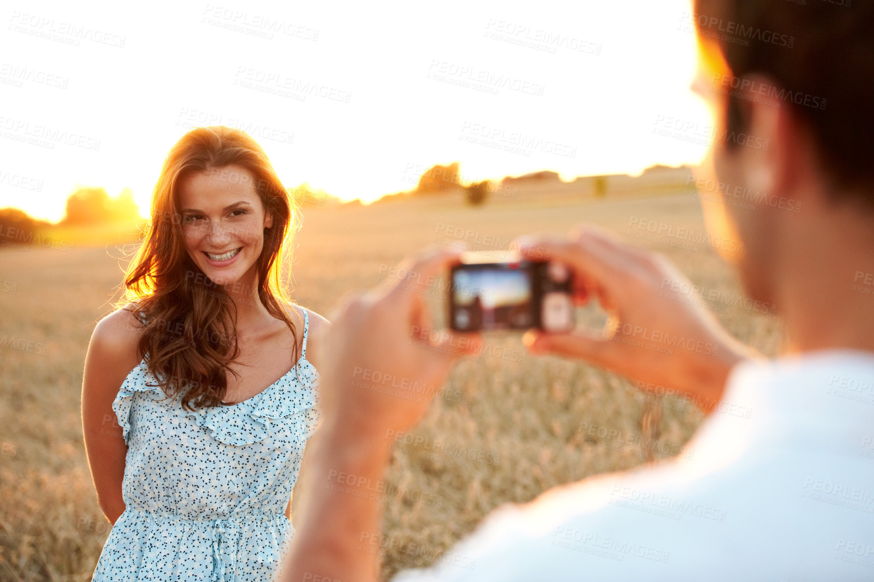 Buy stock photo Woman, sunset and camera with couple in field, photography or memory of honeymoon. Female person, smile and nature with man and digital tech for picture taking, anniversary trip and relationship 