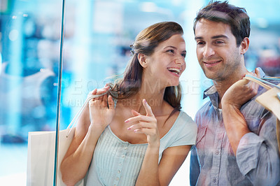 Buy stock photo Couple, smile and window shopping with paper bag in mall, bonding or searching for sale with partner. Boutique, glass and happy people with purchase choice, laughing and pointing at discount deals